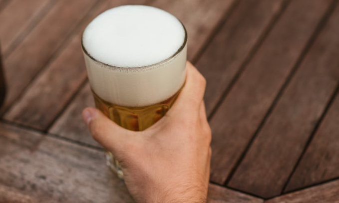 Bier drinken buiten / PEXELS Hand houdt glas bier vast op een houten tafel
