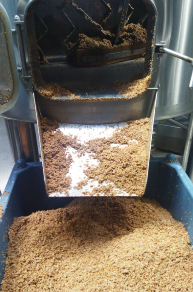 Grondstoffen voor bierproductie uit een metalen vat in een blauwe container.