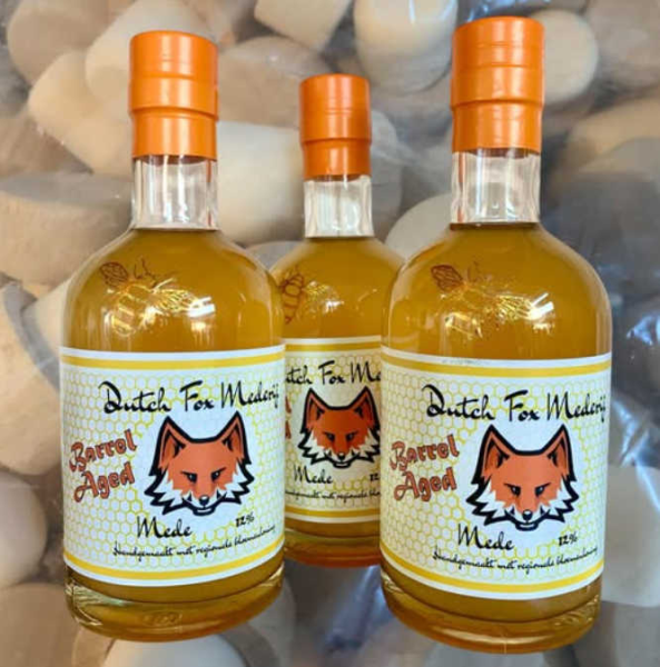 Drie flessen Dutch Fox Mederij honingwijn met oranje doppen en een vos op het etiket.