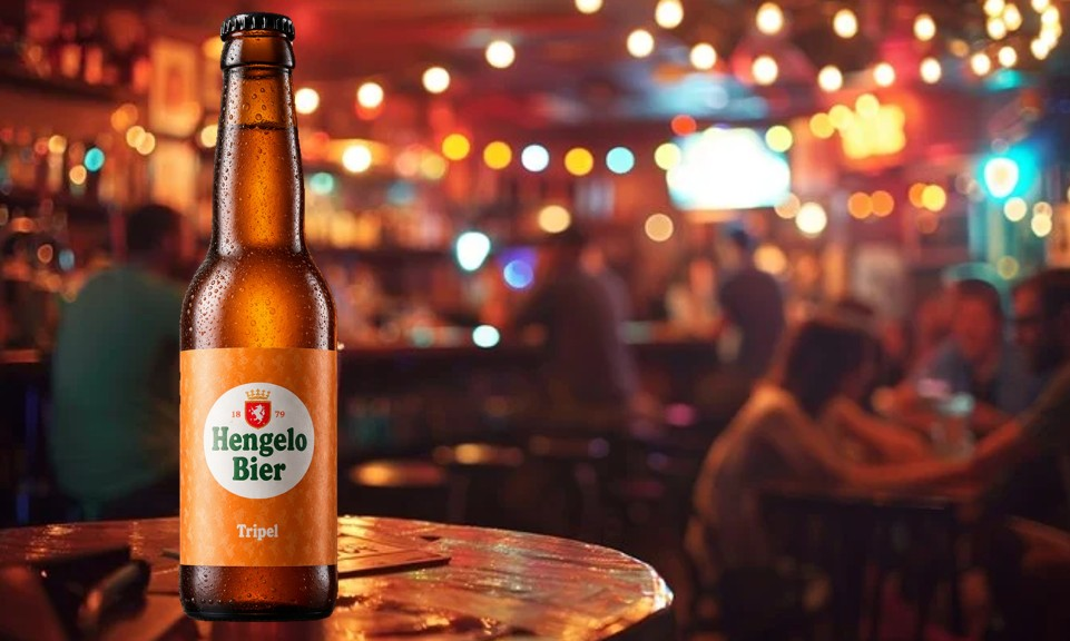 Bierflesje Hengelo Bier op tafel in gezellige bar met mensen op achtergrond.