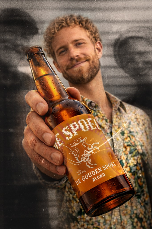 Close-up van een hand met een amberkleurige fles De Spoel tegen een donkere achtergrond.