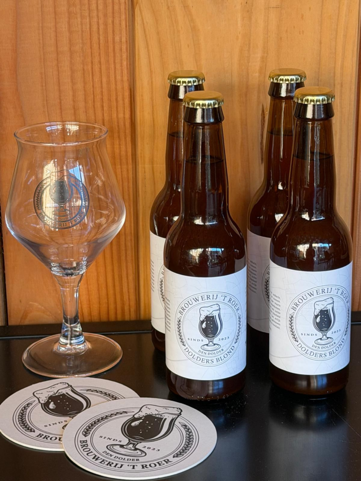 Vier bierflesjes van Brouwerij ’t Roer met proefglas en bierviltjes op een zwarte tafel.