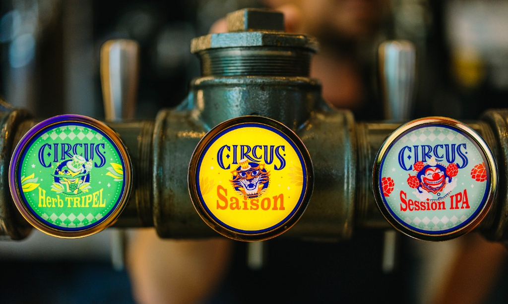 Drie Circus-biertaps met labels voor Herb Tripel, Saison en Session IPA aan een donkere bar.