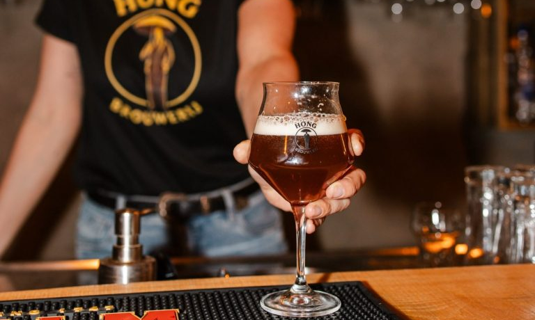 Barman houdt een glas amberkleurig bier met schuim vast achter een bar.