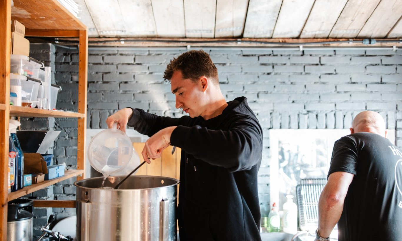 Man giet vloeistof in een grote kookpan en roert in een industriële keuken.