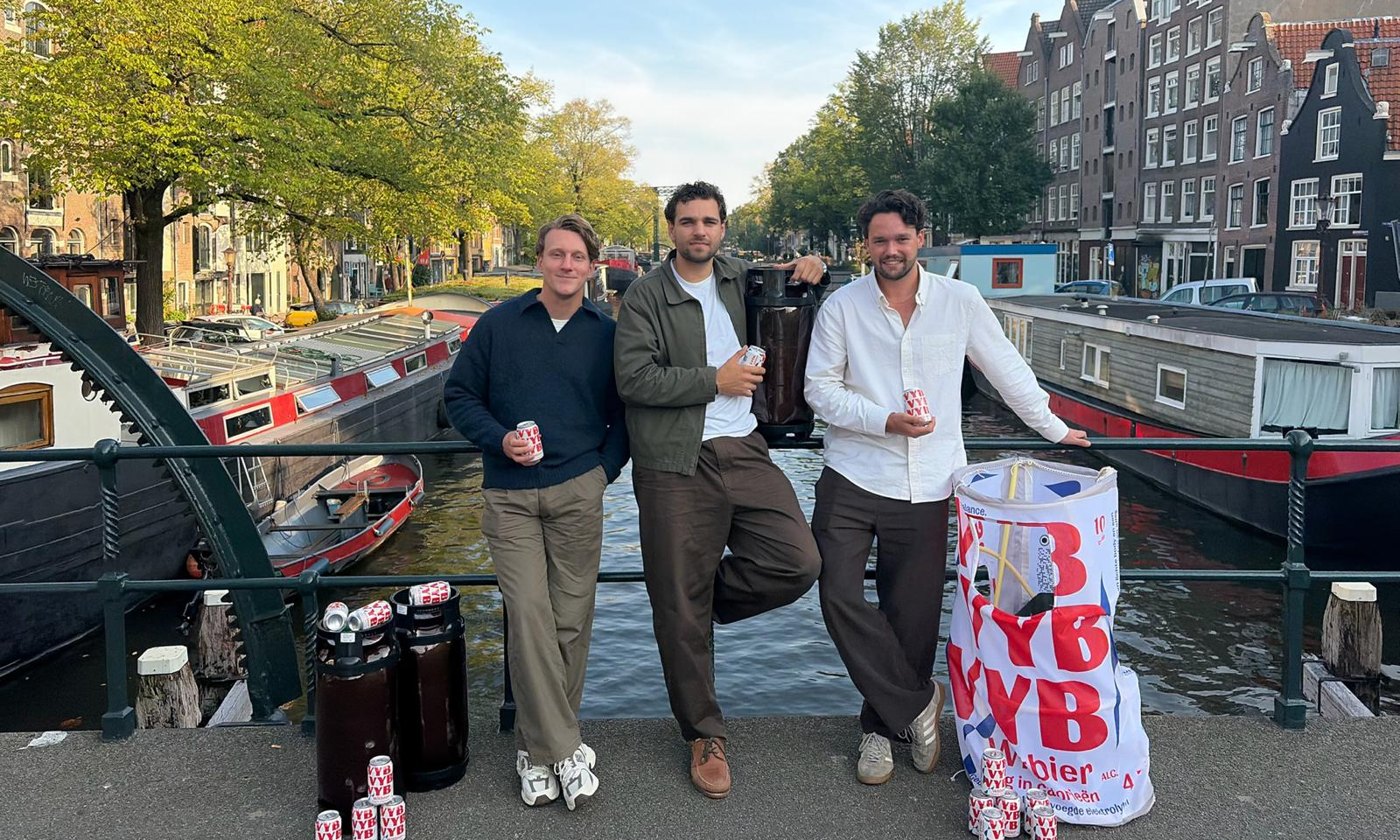Cas, Merijn en Ben op een brug boven een Amsterdamse gracht met blikjes en promotiemateriaal van VYB.