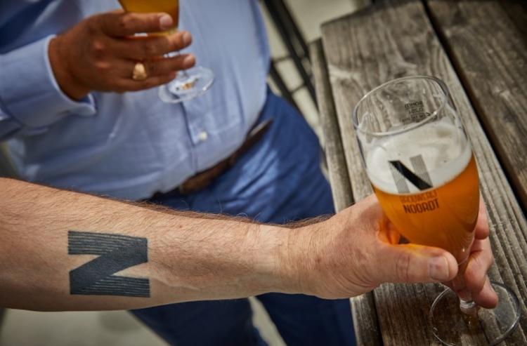 Man met een Brouwerij Noordt tattoo op zijn arm houdt een glas bier van de brouwerij vast