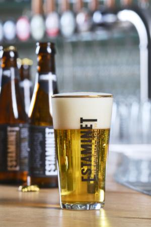 Estaminet Refined Lager vol glas met flesjes op de achtergrond