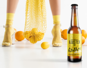 Bjuster Radler 10% flesje met vrouw erachter met een netje citroenen