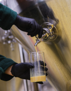 Drankje wordt uit de lagertank getapt door personeel met zwarte handschoenen aan.