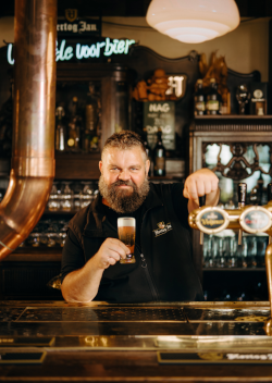 Meesterbrouwer Micha Peute van Hertog Jan achter de bar met een glas pils in de hand