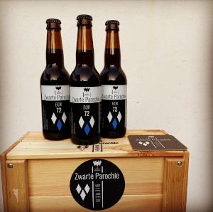 Drie Zwarte Parochie Bieren op een kistje met een sticker van de brouwerij erop