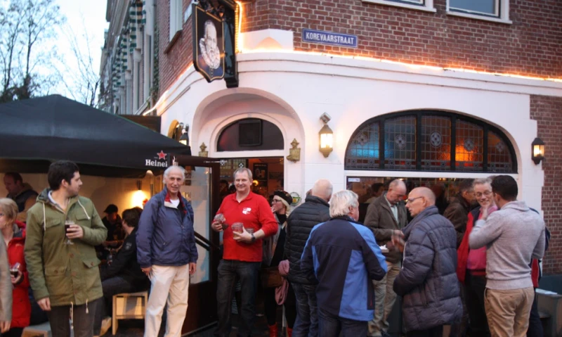 Groep mensen staand voor een hoekcafé op een stadsstraat tijdens avondwandeling
