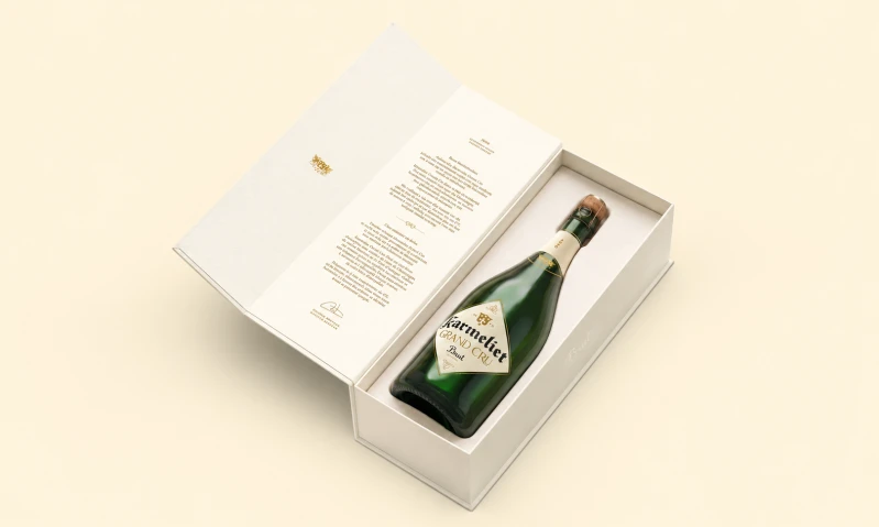Groene fles Karmeliet Grand Cru Brut in open witte cadeauverpakking op crèmekleurige achtergrond