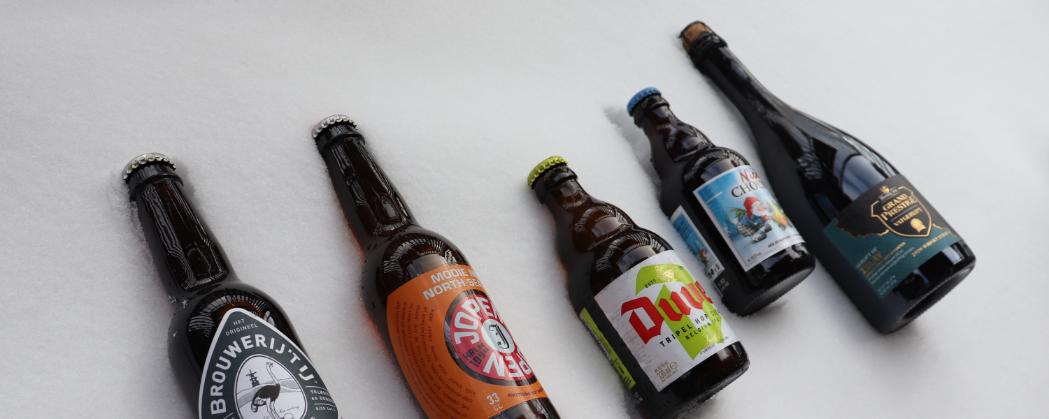 Vijf bierflessen liggen horizontaal in de sneeuw, van links naar rechts in een licht gebogen lijn.