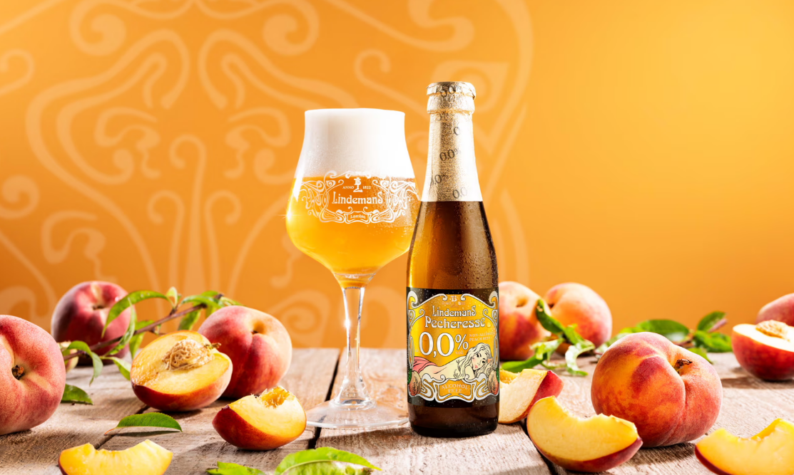Lindemans Pecheresse 0,0% bier flesje en glas tussen perzikken in Lindemans Pecheresse 0,0% bier flesje en glas tussen perzikken in