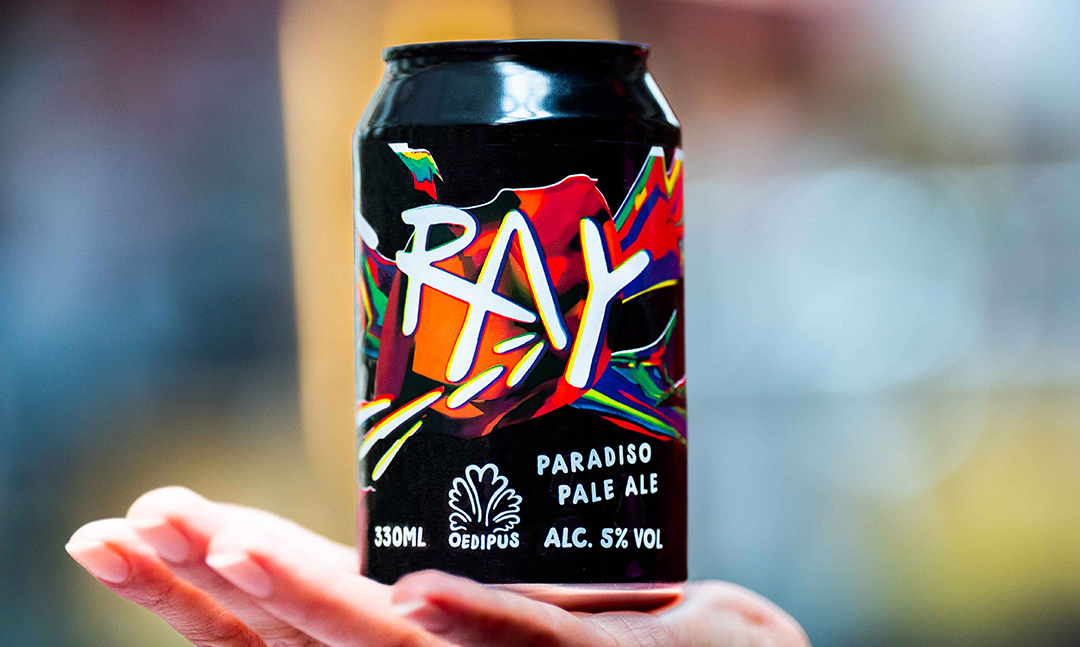 Een hand houdt een blik van Oedipus RAY paradiso pale ale vast voor een muur.