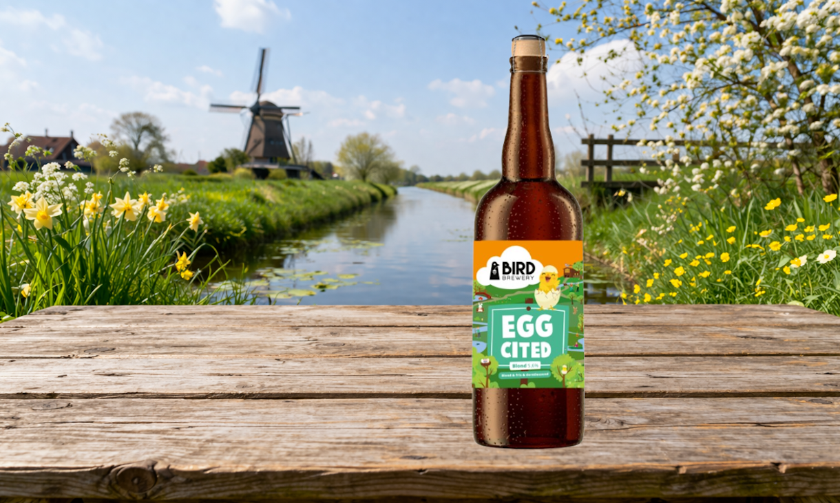 Fles Bird Eggcited 2026 op houten tafel bij bloemen en molen langs kanaal.