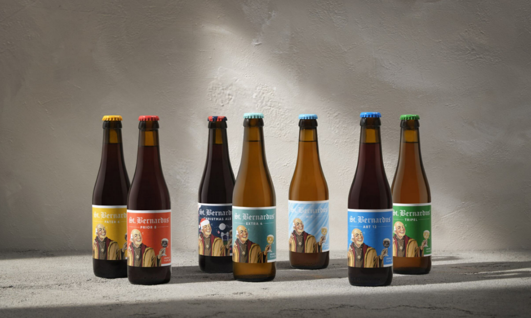Zeven St. Bernardus bierflesjes in verschillende kleuren op betonnen oppervlak.