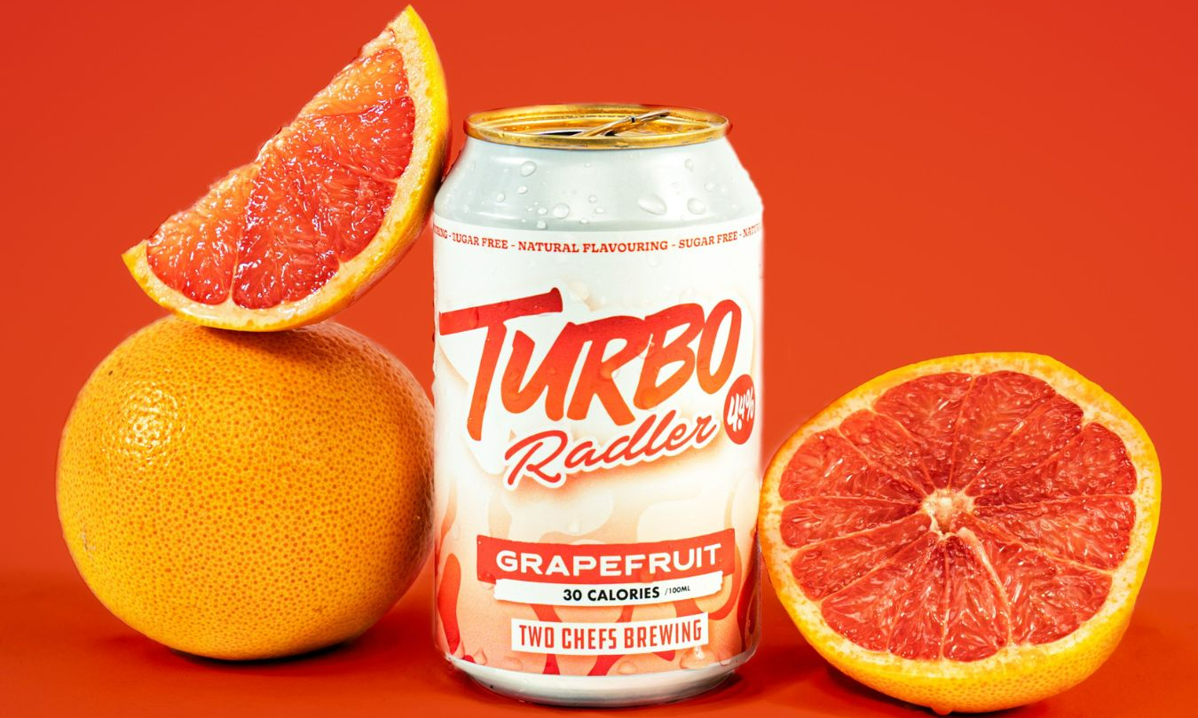 Een blik Two Chefs Turbo Radler Grapefruit met halve en hele grapefruits op een oranje achtergrond.