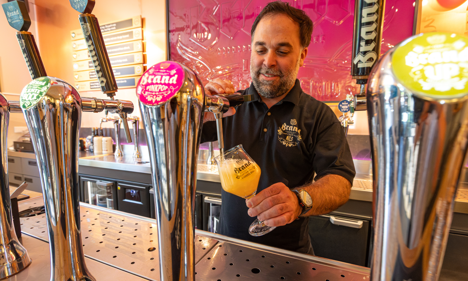 Man tapt bier in een glas achter een bar, met meerdere bierkranen zichtbaar.