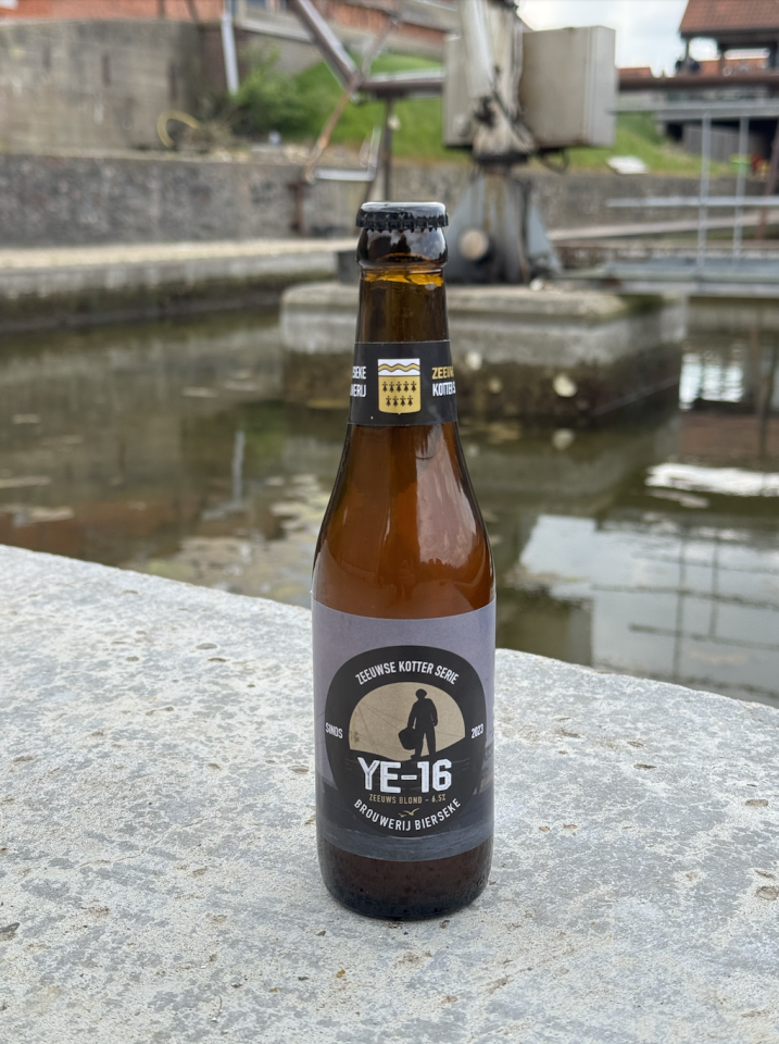 Flesje YE-16 Zeeuws Blond bier op een betonnen rand bij een watergang.