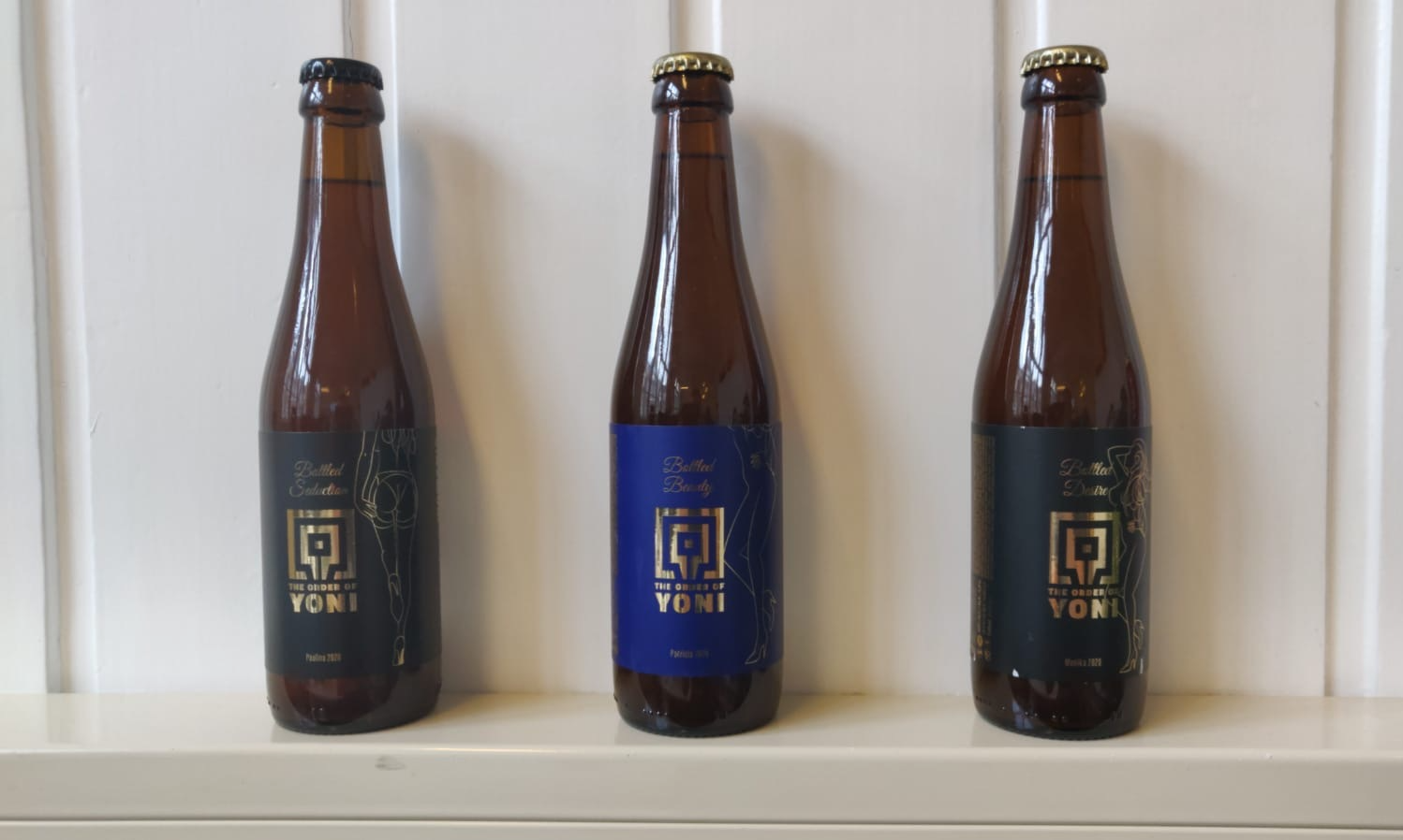 Drie bruine flessen van The Order of Yoni op een witte vensterbank tegen een lichte wand.