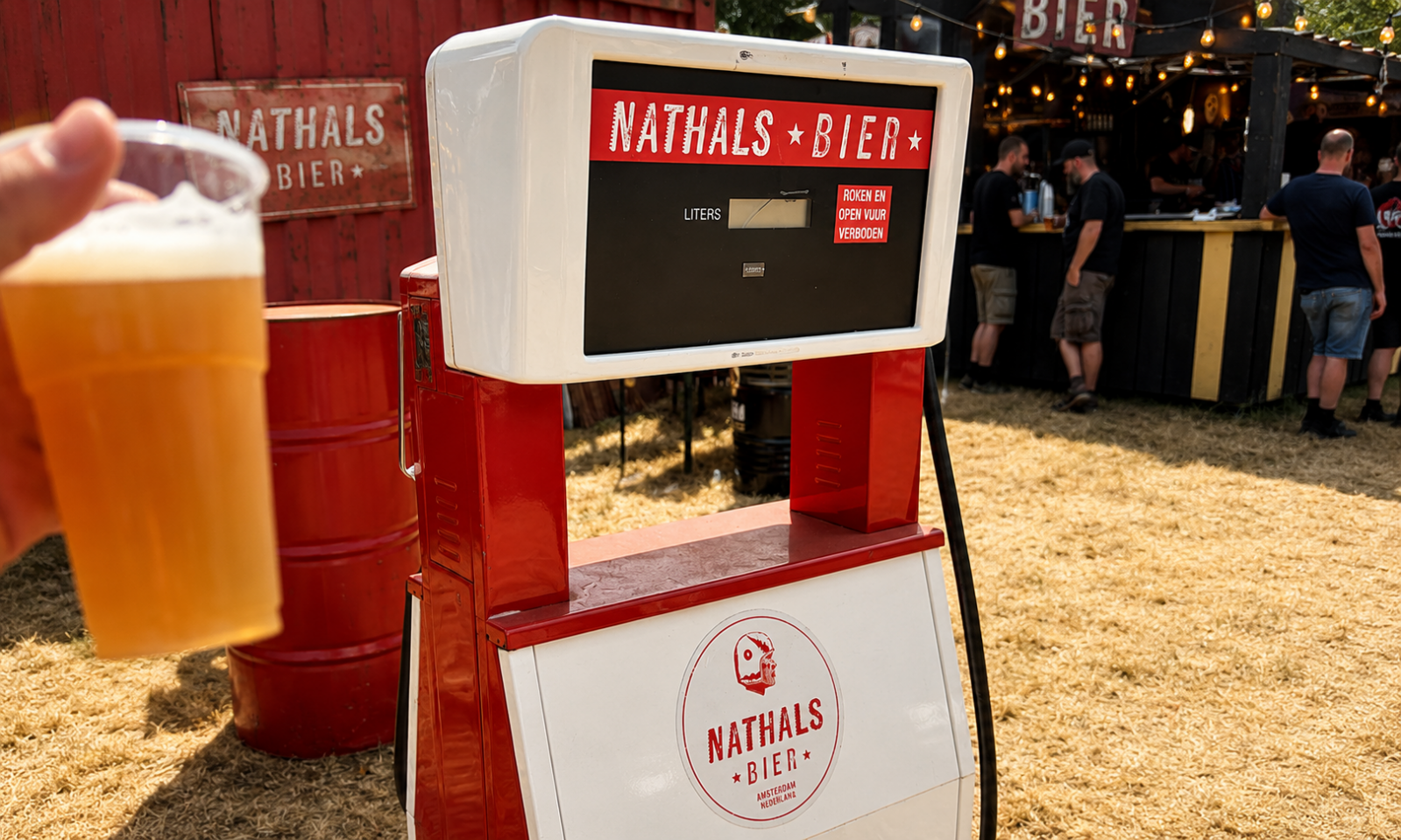 Retro Nathals bierpomp met plastic bierglas op een zonnig festivalterrein bij een bar.