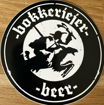 Rond zwart-wit Bokkeriejer Beer-logo op een houten tafel met silhouet van een ruiter op een bok.