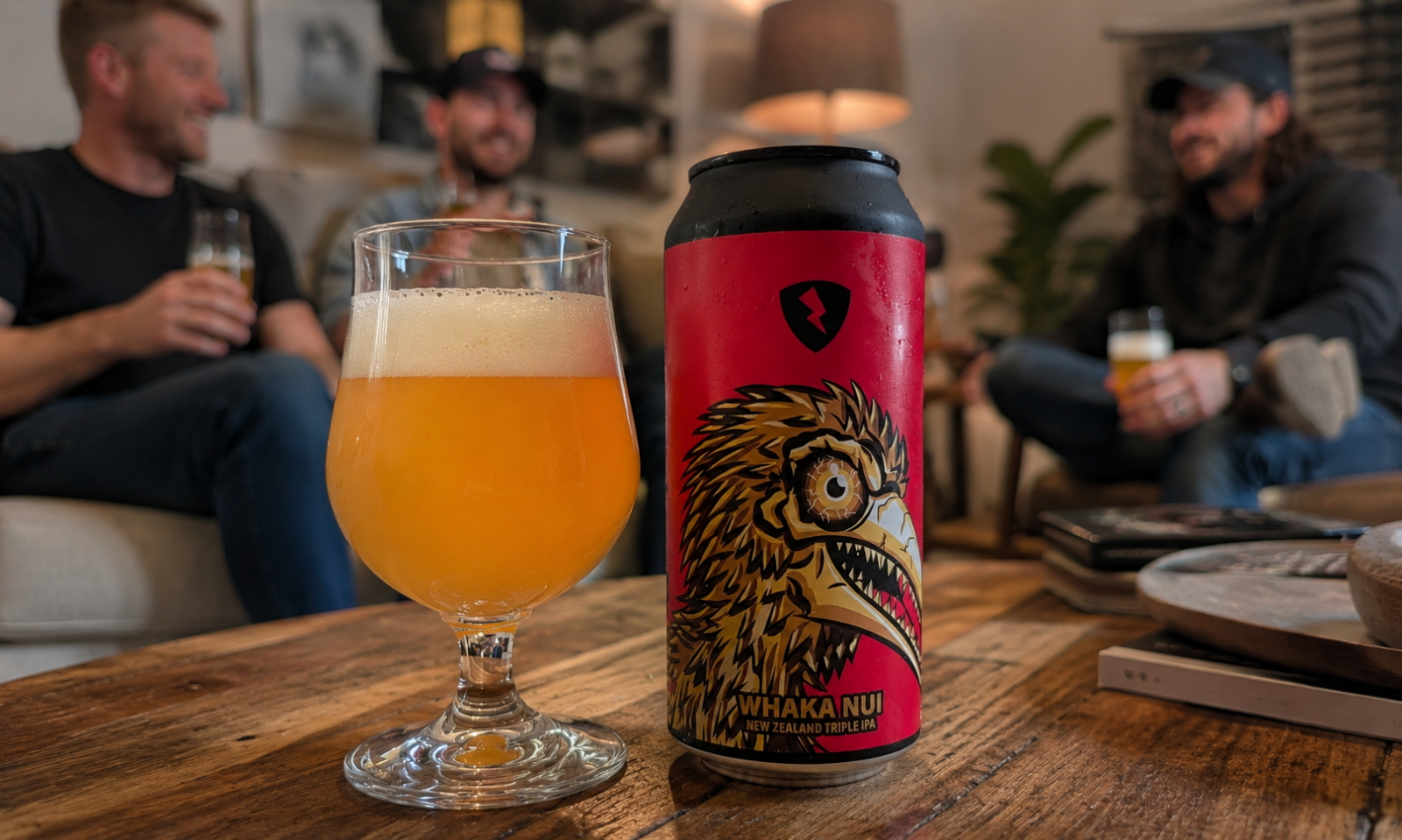 Blik Rock City Whaka Nui en glas hazy bier op houten tafel met vrienden op de achtergrond.