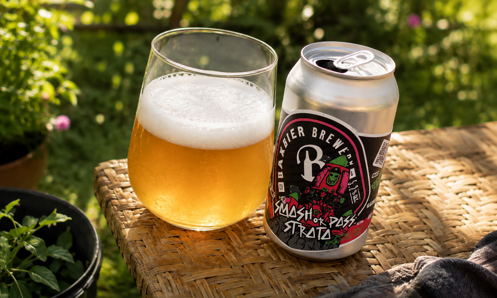 Blik Baxbier Smash or Pass Strata naast een glas goudkleurig bier op een rieten tafel in de tuin.