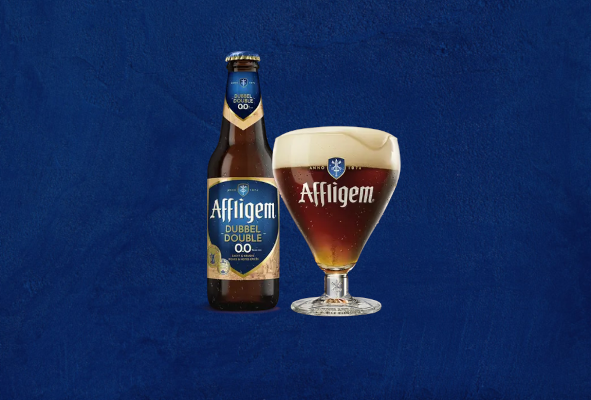 Affligem Dubbel 0.0% fles en gevuld bierglas met schuim op een donkerblauwe achtergrond.