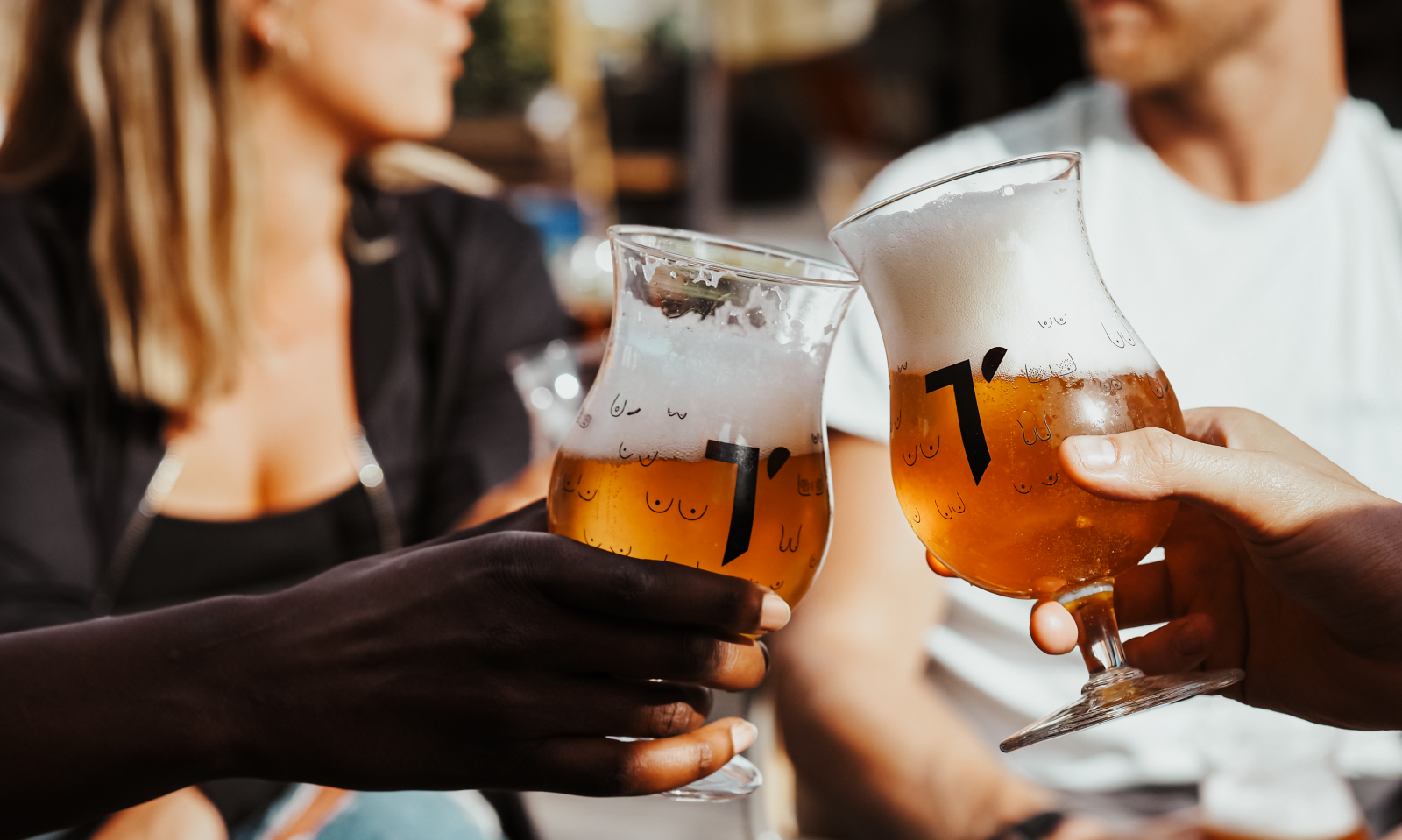 Vrienden proosten buiten met bolle glazen amberkleurig bier met schuimkraag.