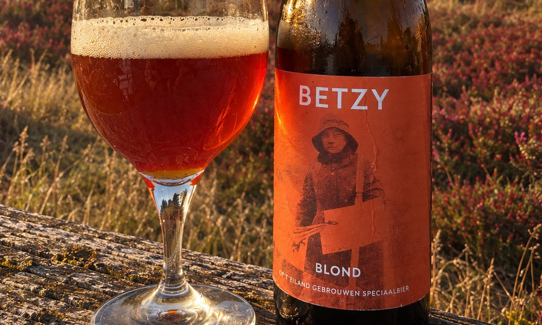 Glaasje amberkleurig bier en fles Betzy Blond op houten bankje in heide bij gouden licht