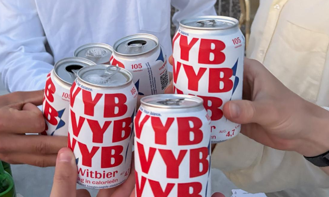 Vriendengroep proost met meerdere witbierblikken boven een tafel met speelkaarten (dakterras).