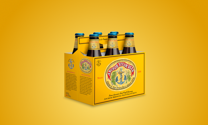 Zes flesjes Anchor Steam bier in een gele kartonnen verpakking.