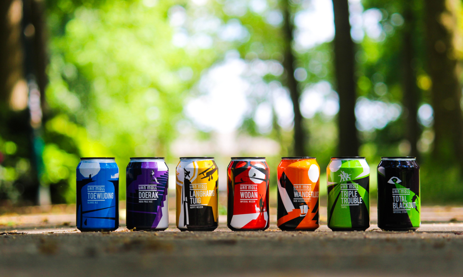 Zeven kleurrijke bierblikken met creatieve ontwerpen staan naast elkaar op een buitenlocatie.