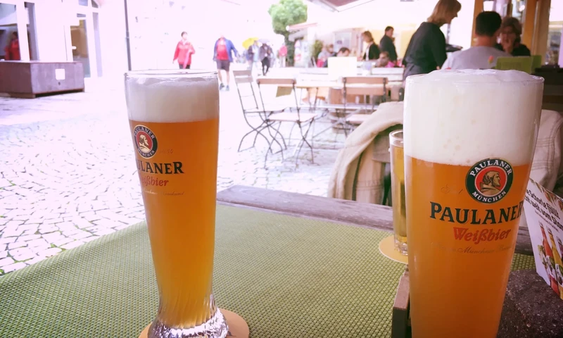 Twee glazen Paulaner Weissbier op een tafel van een terras.