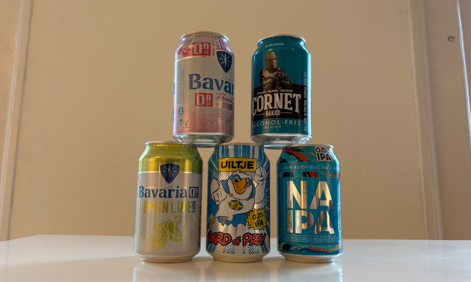 Stapel van vijf blikjes alcoholvrij bier op een witte tafel.
