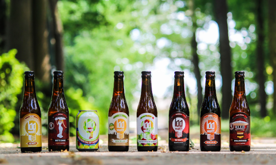 Zeven bierflessen en een blikje van Lighttown Brewers in een bosrijke omgeving.