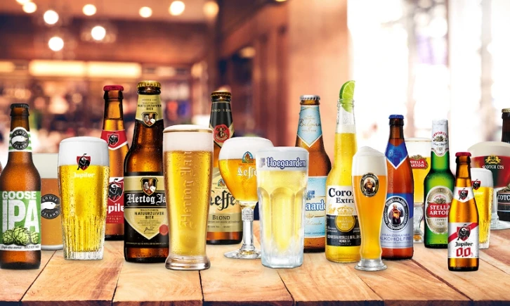 Rij met verschillende bierflessen en -glazen, o.a. Goose IPA en Leffe, op houten tafel in café-setting.