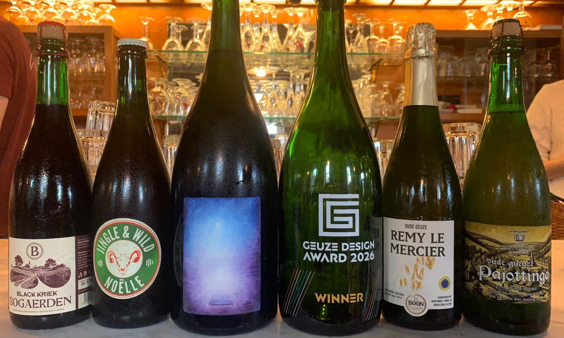 Een rij bierflessen op een bar, met in het midden een bekroonde fles van de Geuze Design Award 2026.