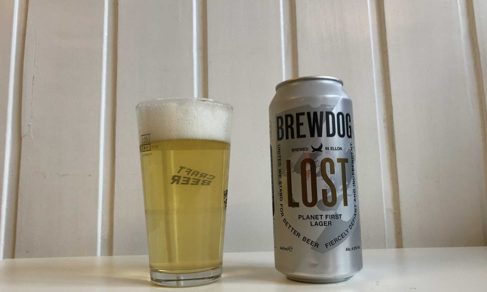 BrewDog Lost bierblik naast een glas gevuld met bier tegen witte achtergrond.