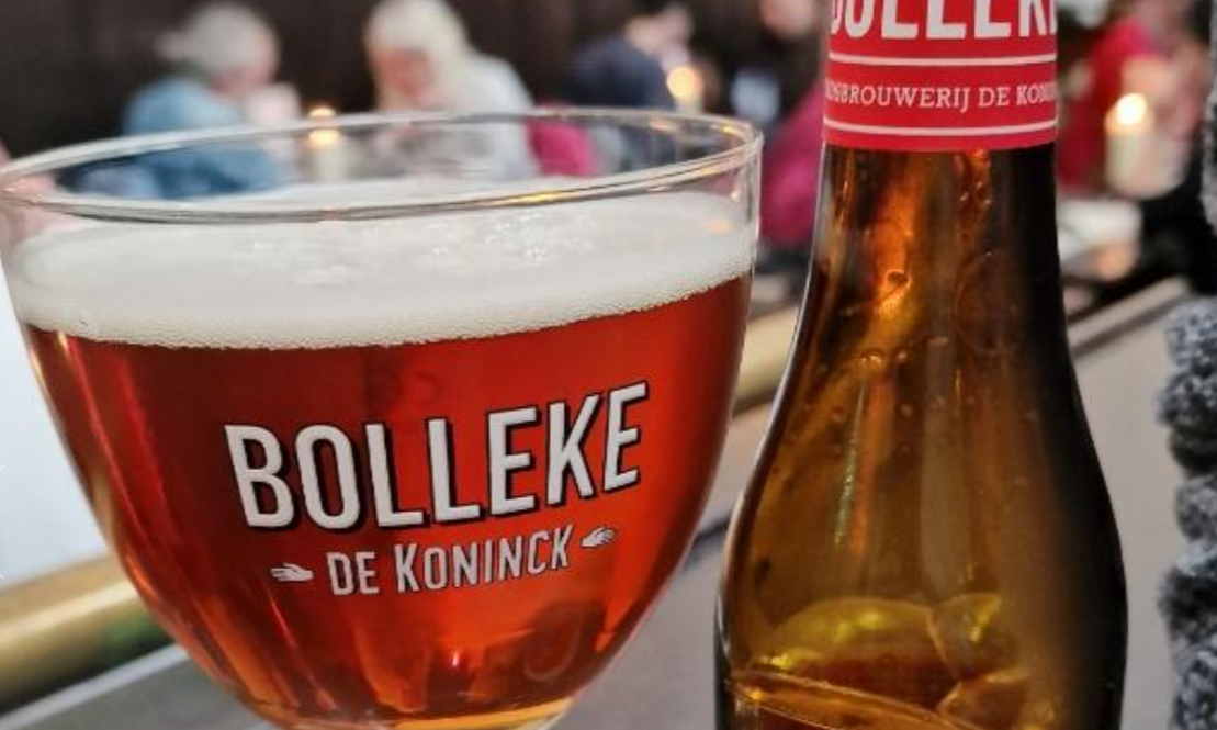 Glas Bollleke bier naast een Bollleke bierflesje in een café omgeving.