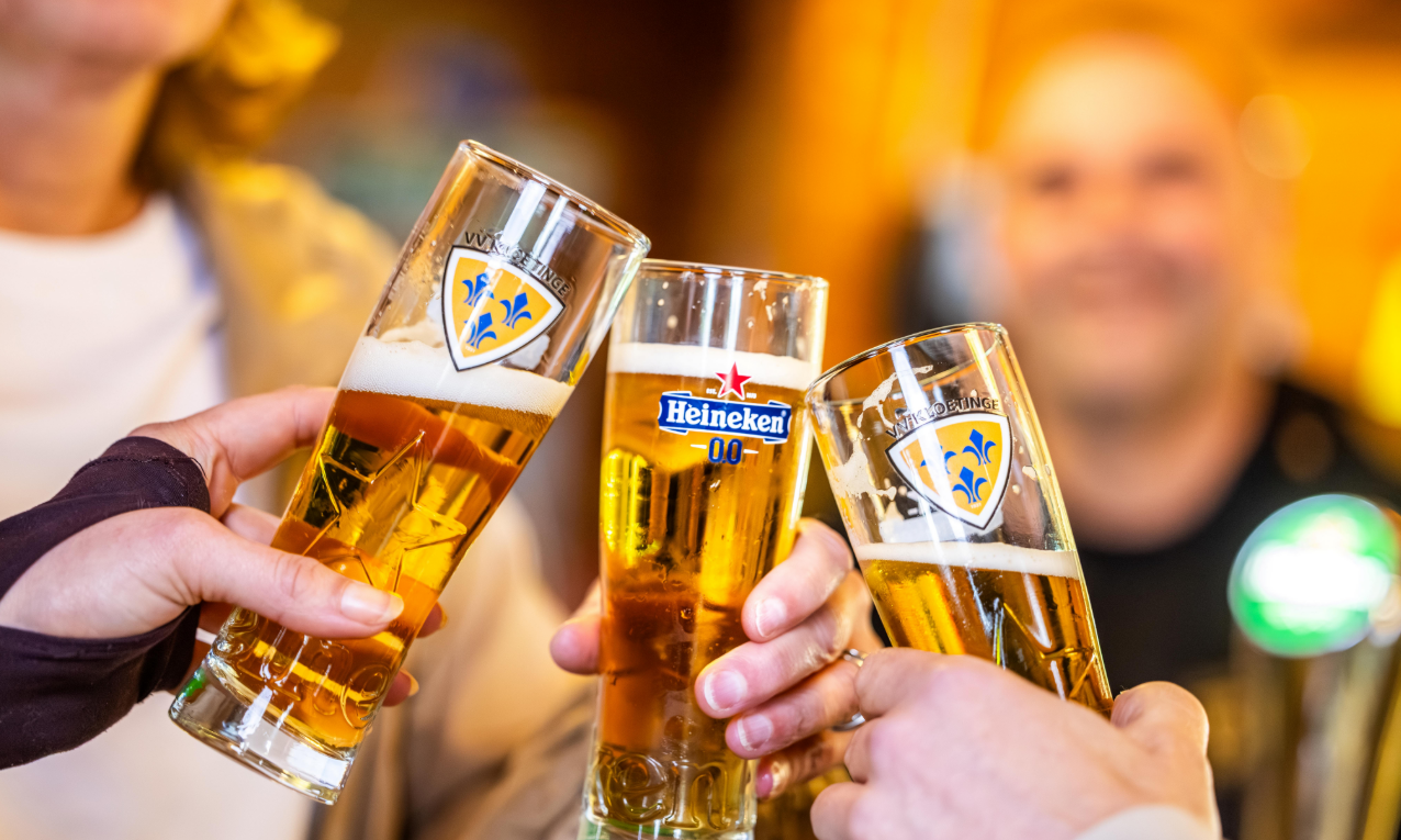 Drie mensen proosten met glazen gevuld met Heineken 0.0 bier met glazen met het logo van VV Kloetinge
