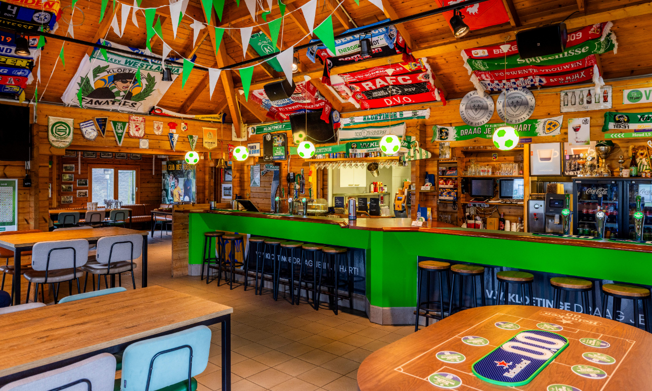 De voetbalkantine van VV Kloetinge met groene accenten, versierd met voetbalvlaggen en borden.