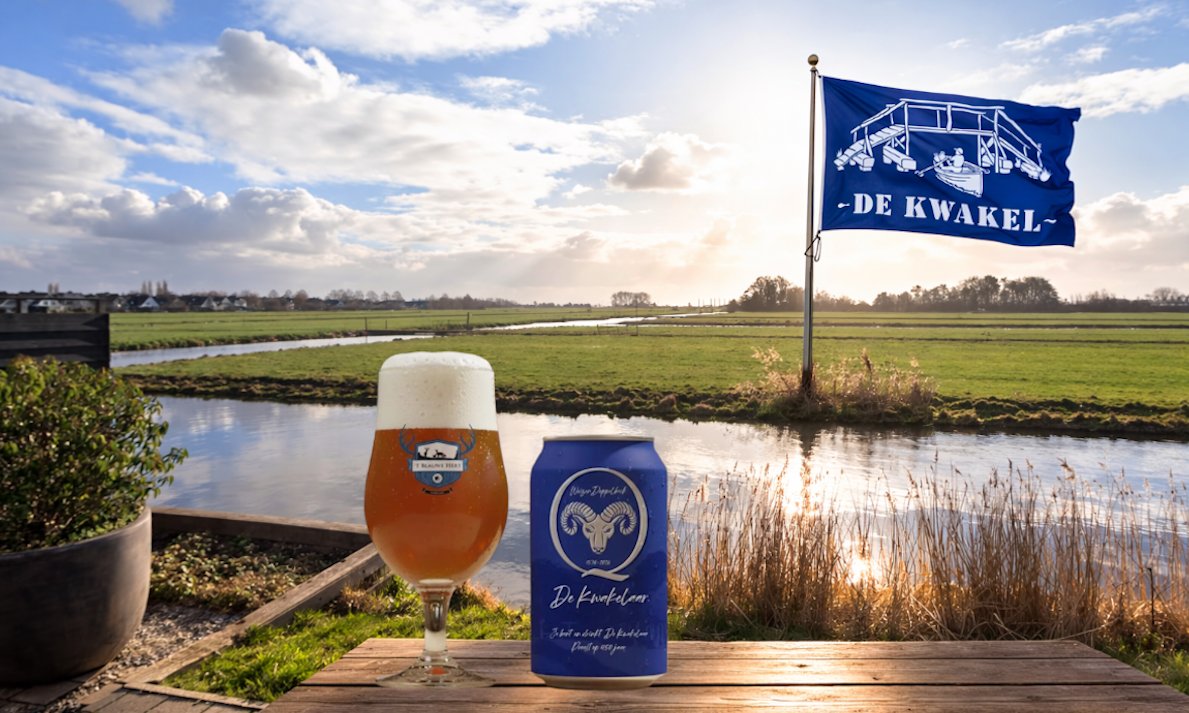 Glas en blik Kwakel jubileumbier op houten tafel met vlag op achtergrond.