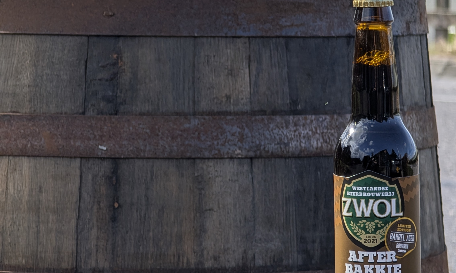 Een fles Afterbakkie Barrel Aged bier van ZWOL voor een houten vat.