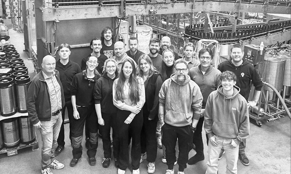 Groepsfoto van medewerkers in fabriek, omringd door industriële apparatuur.