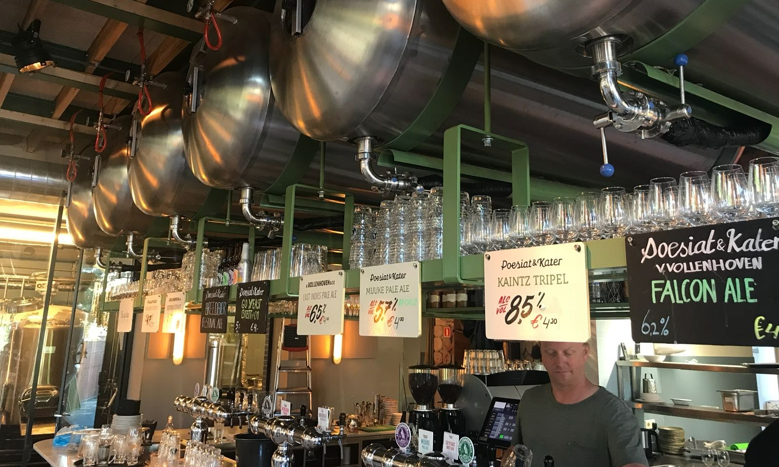 Barmanager bij Poesiat & Kater onder grote metalen biertanks in een moderne brewpub.